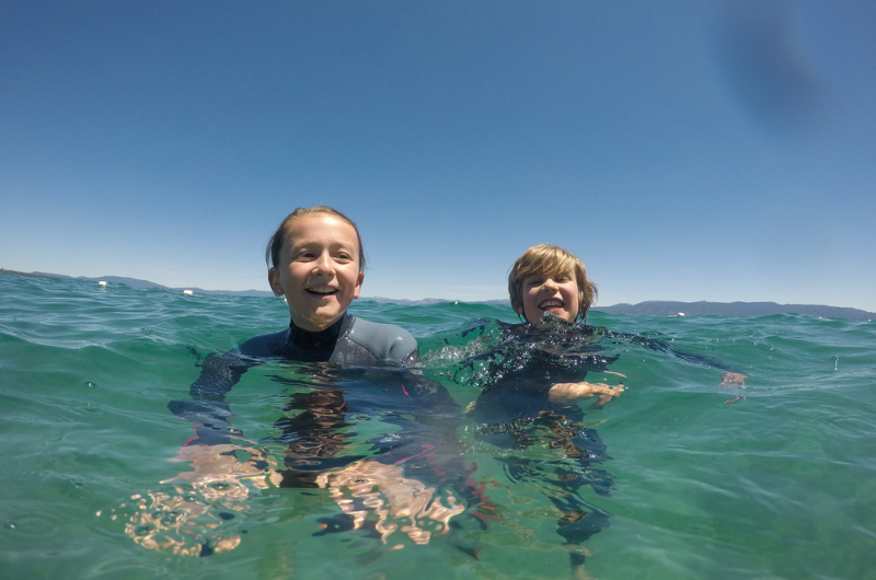 Two children happily swim in an open body of water.