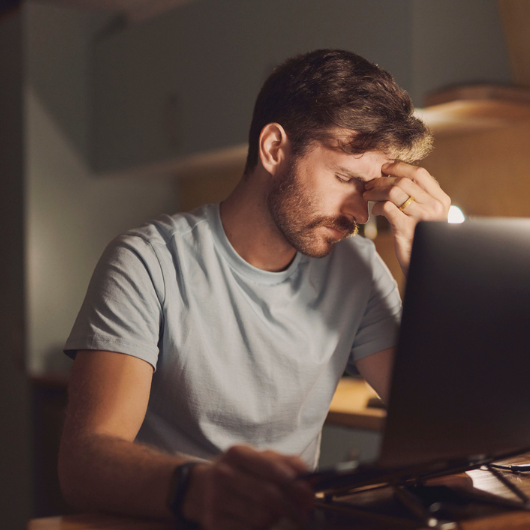 Man sitting in front of a desktop computer looking stressed, putting his hand on his forehead.