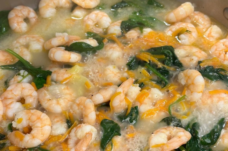 A pot of shrimp and greens cooks on the stove.