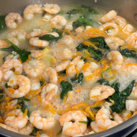 A pot of shrimp and greens cooks on the stove.
