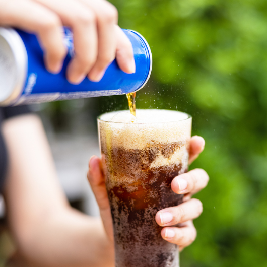 Female hand pouring a diet soda drink from a can to a glass.