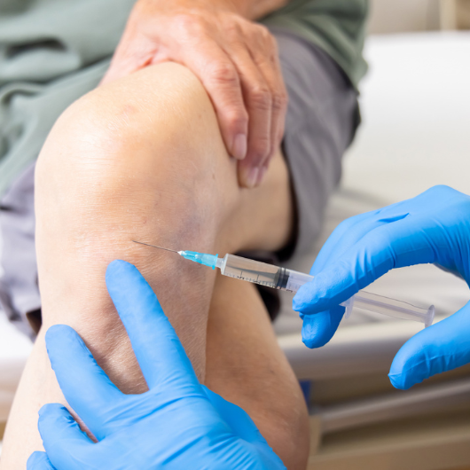 A gloved doctor prepares for a PRP injection in a patient’s knee.