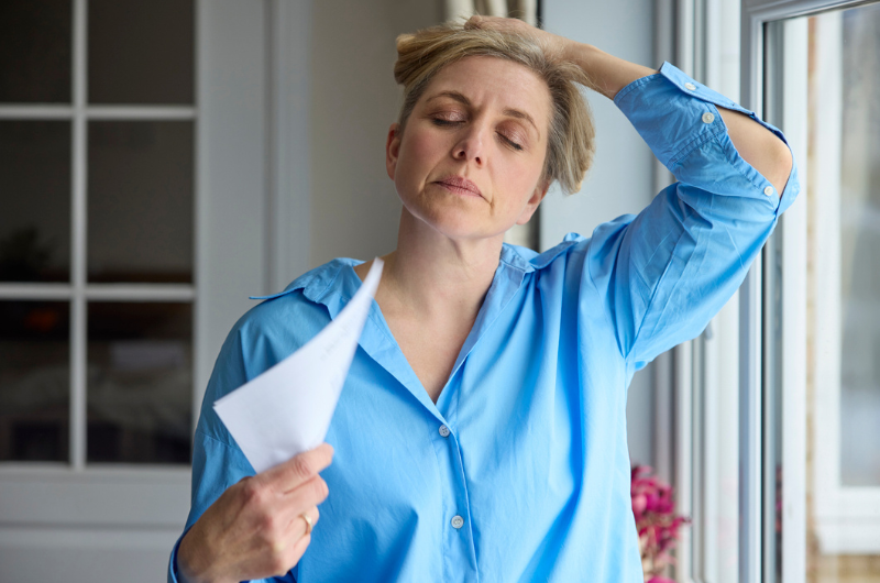 A menopausal woman having a hot flash while fanning herself with paper.