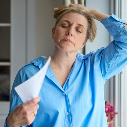 A menopausal woman having a hot flash while fanning herself with paper.