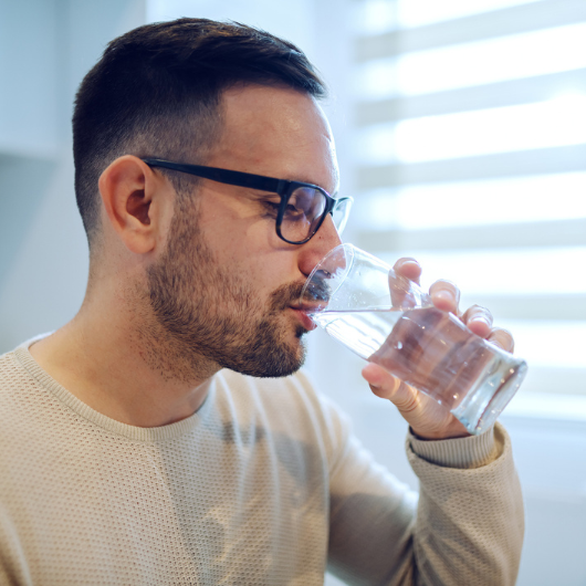 Side view of a Caucasian man sitting at a dining table drinking a glass of water.
