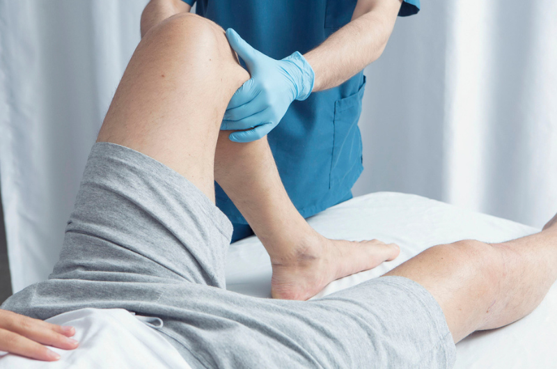 A physician wearing gloves examines a patient's knee.