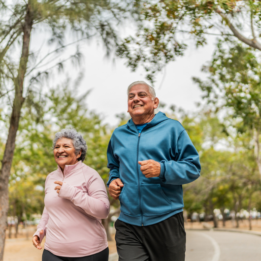 Older man and woman happily walk outside along a tree-lined path.