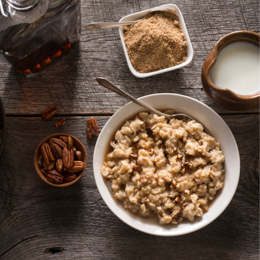 Top-down view of two bowls of oatmeal with side dishes of pecans and brown sugar. 