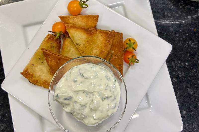 Top-down view of a plate of garlic rosemary pita chips and herb drip. 