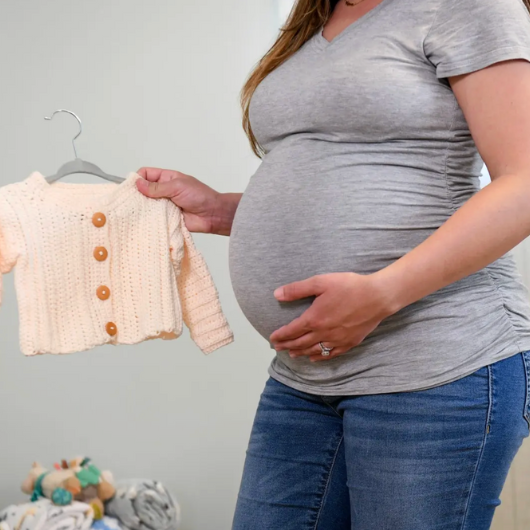 A pregnant woman holding a small sweater and touching her belly.