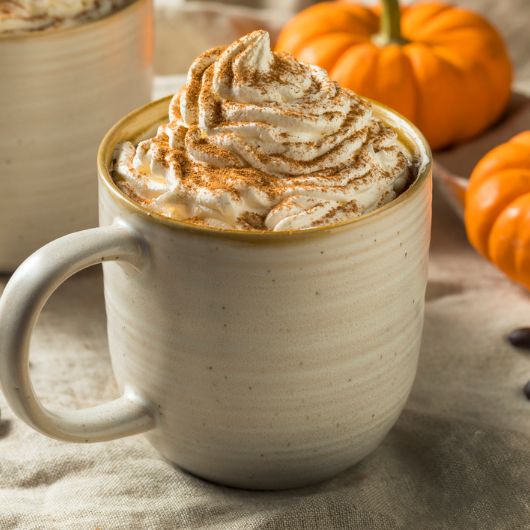A coffee mug filled with a pumpkin spiced latte sits on a table. 