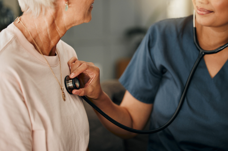 Doctor and senior woman consulting about heart screenings on living room sofa in retirement home.