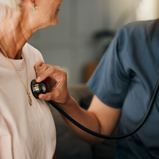 Doctor and senior woman consulting about heart screenings on living room sofa in retirement home.