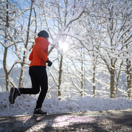 Female athlete jogs on a road with slush and snow in background.