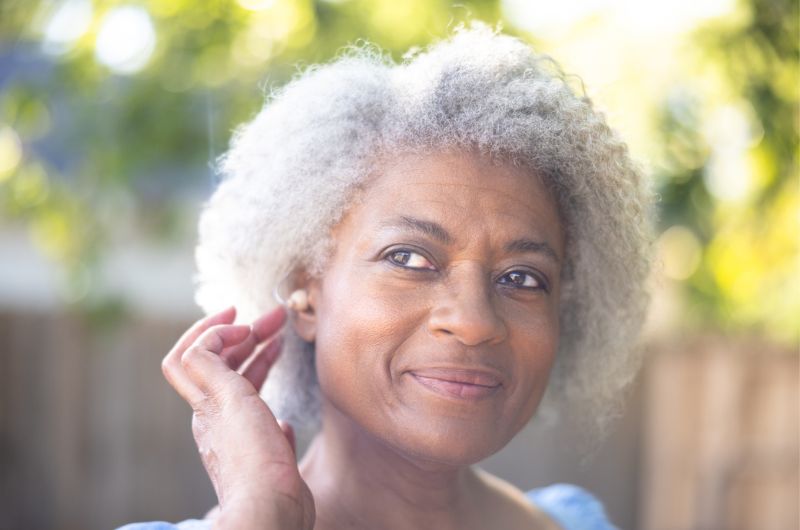 Older African American woman lightly touches her ear.