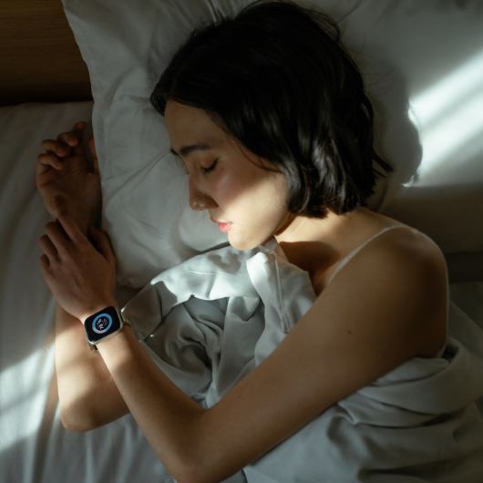 Woman sleeping peacefully in bed, wearing a smart watch to track her sleep patterns.