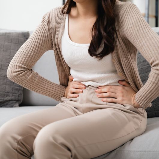 Image shows a close up of a woman holding her lower stomach while sitting on a couch.