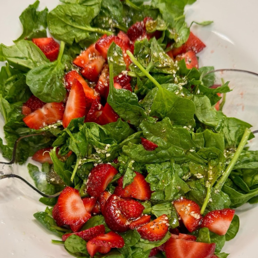 A healthy salad featuring ripe strawberries and fresh spinach.