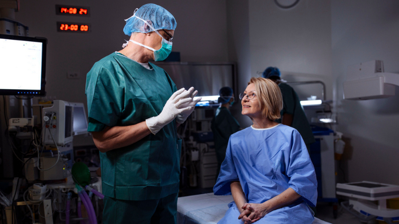 Surgeon speaks with a calm, smiling patient in a preoperative hospital room before surgery.