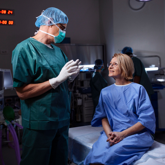 Surgeon speaks with a calm, smiling patient in a preoperative hospital room before surgery.