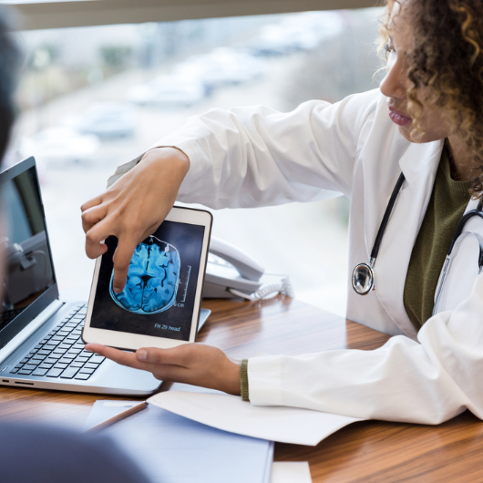 A middle-aged female doctor holds a digital tablet displaying the brain scan.