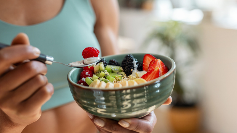 Close up of athletic woman eating a healthy fruit bowl in the kitchen at home.