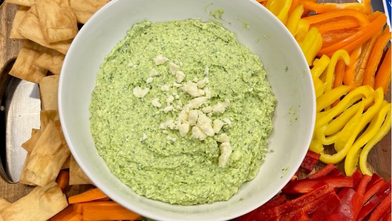 Top-down view of green goddess whipped feta dip surrounded by slice veggies and crackers. 