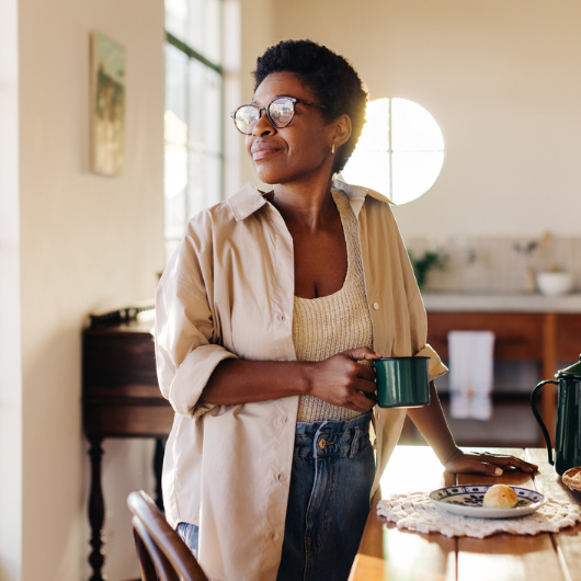 Thoughtful Brazilian woman looking away while holding a cup of coffee in her kitchen.