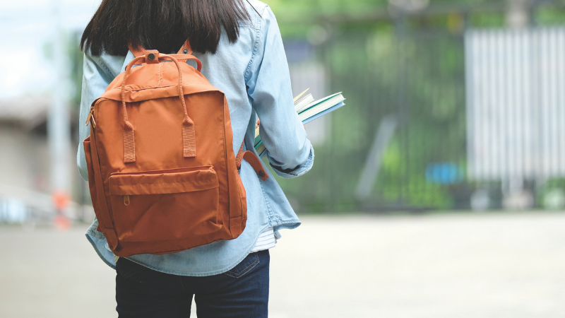 Student walking carrying notebooks and wearing backpack