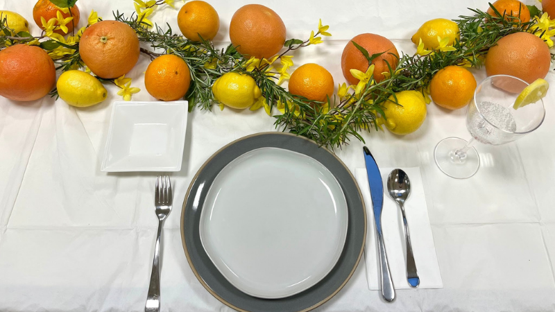 Top-down view of a decorated tablescape with a citrus and yellow floral garland.