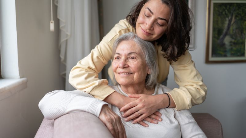 Daughter hugging her senior mother from behind.
