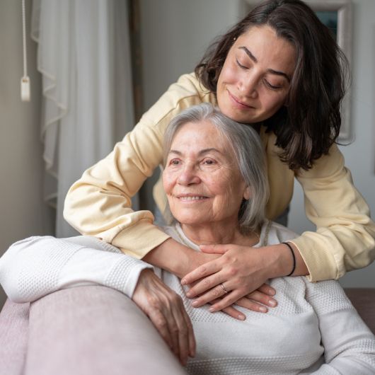 Daughter hugging her senior mother from behind.