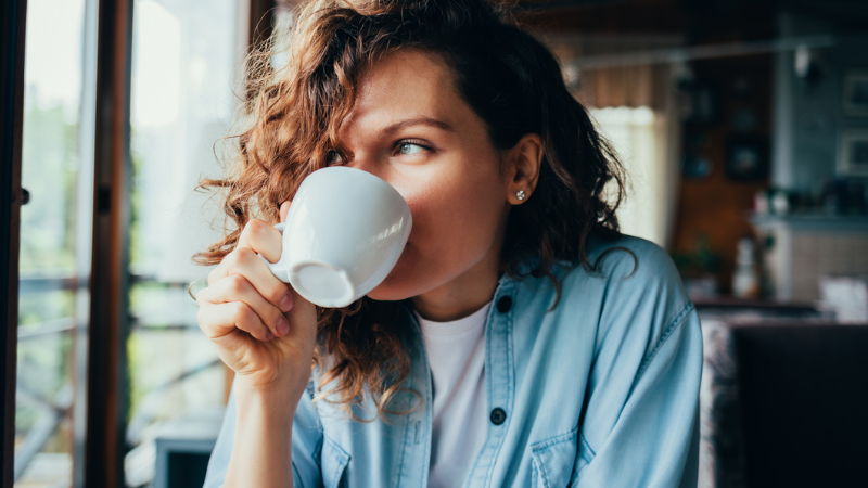 Portrait of a happy, beautiful young woman wearing a blue shirt and drinking coffee.