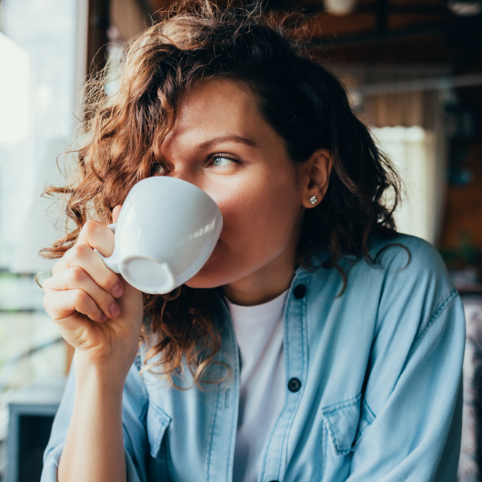 Portrait of a happy, beautiful young woman wearing a blue shirt and drinking coffee.