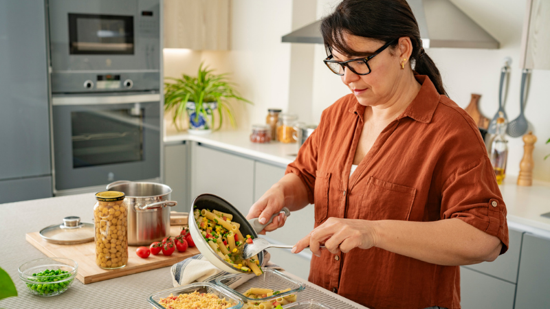Woman in the kitchen preparing healthy homemade weekly meals in glass containers.