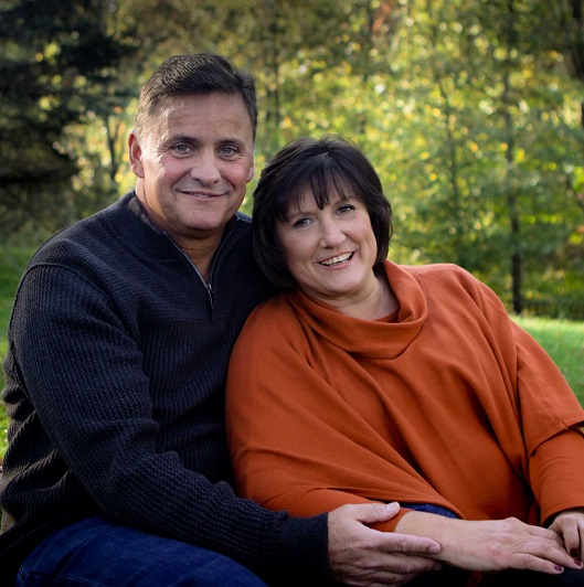 Mike Hennessy and his wife Patti, sitting together hugging and smiling.
