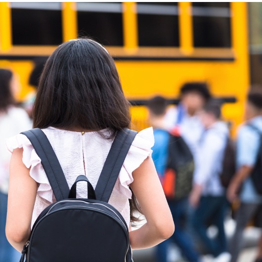 A female middle school student walks hesitantly to the school bus on the first day of school.