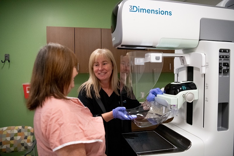 Nurse standing with patient in front of a mammogram machine.
