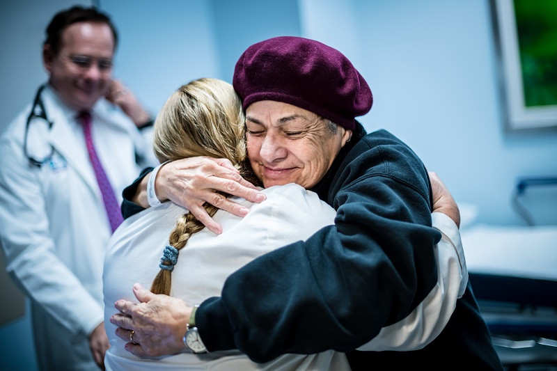 A patient hugging one of their nurses, while their doctor is smiling in the background.