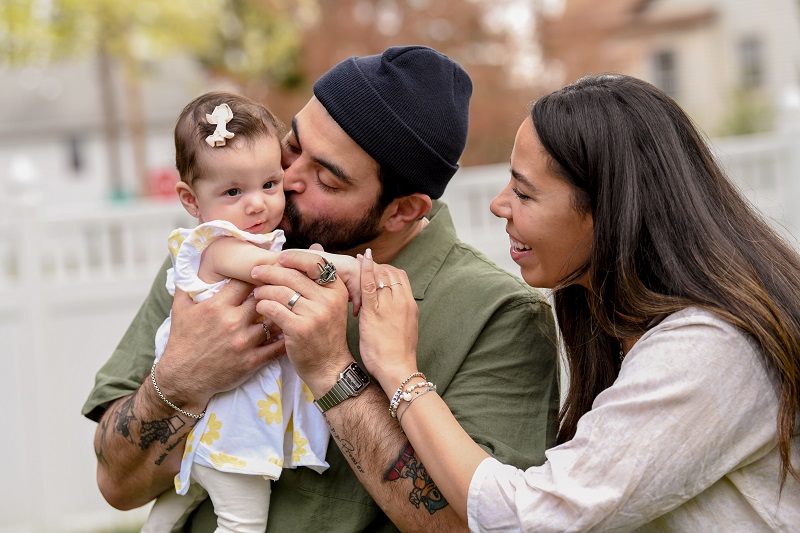 Baby Lola Prieto getting a kiss from her dad, Victor, with mom, Sasha smiling and holding her hand.