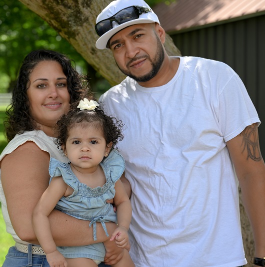 A mother, father and daughter, the Lopez family, smiling in the park.