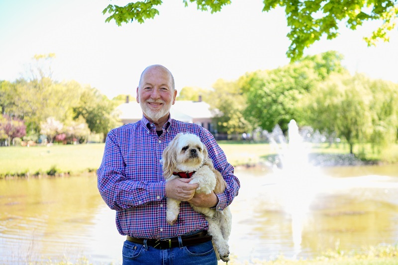 Patient Dan Reiss, holding his dog, Jake, smiling outside.