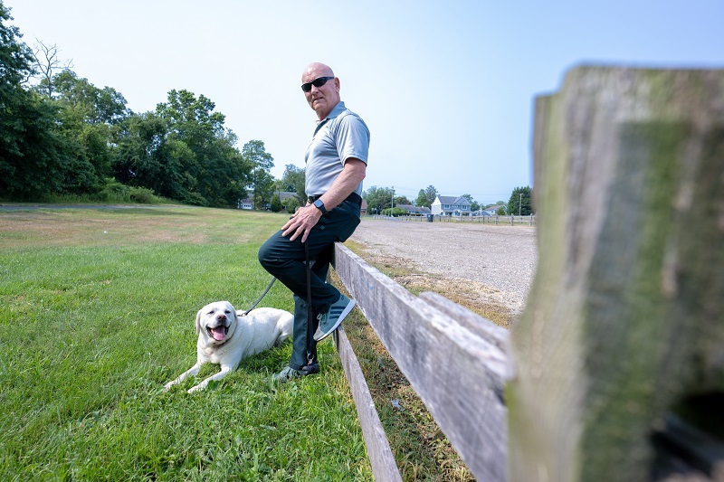 Man stands up against a fence with his yellow lab.
