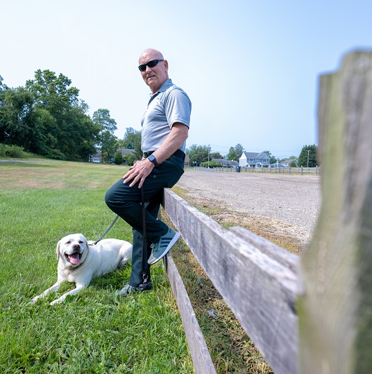 Man stands up against a fence with his yellow lab.