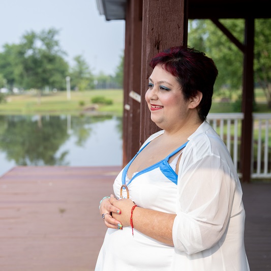 Woman stands on a dock looking out at the water smiling.