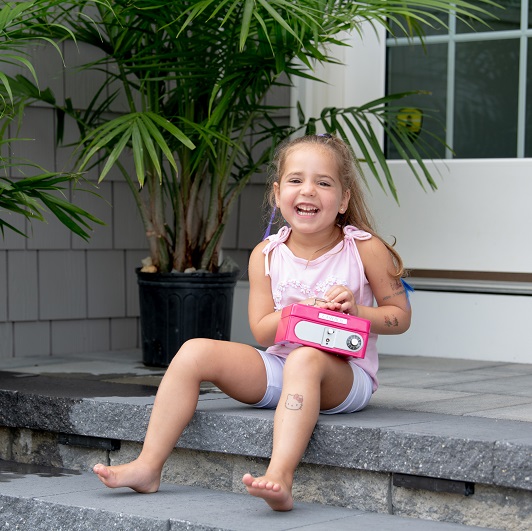 Toddler Maddie Troeller smiling on the front step with her piggy bank.