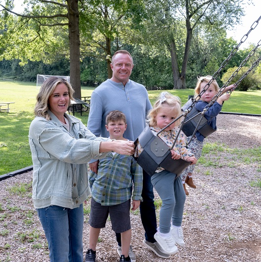 Trista Harper and her family smiling, enjoying the park. Riding bikes, pushing the stroller, and swinging on the swings.