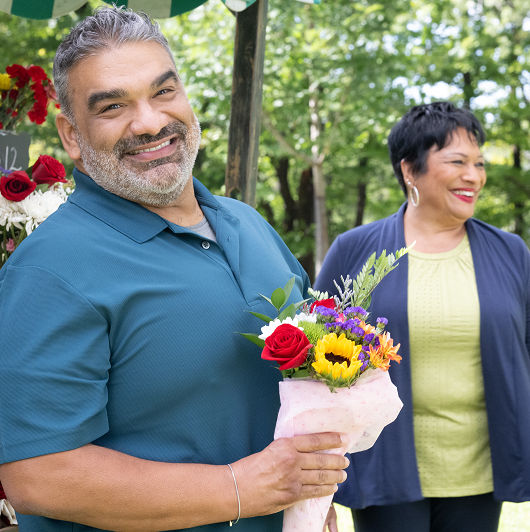 Carlos Mercado holding a bouquet of flowers smiling.