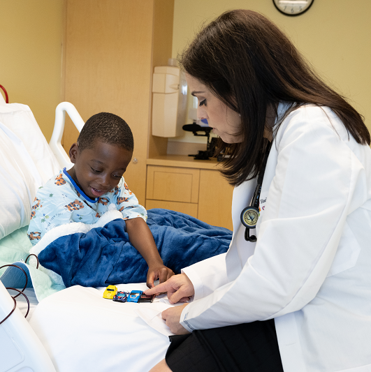 Stacey Rifkin-Zenenberg, D.O. and patient Tobi playing with toy cars on his patient bed.