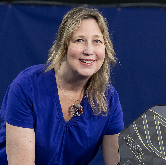 Diane Blaszka holding a pickleball racket, ready to play and smiling.